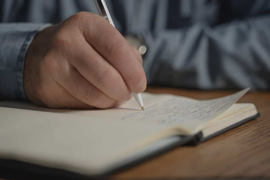 Gros plan d'une main écrivant au stylo dans un carnet, rédigeant une note personnelle.