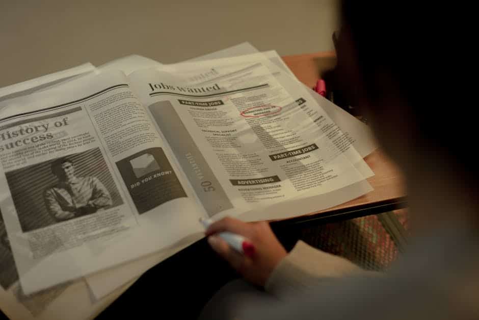 Une personne consulte des offres d'emploi dans un journal, surligneur rose à la main.