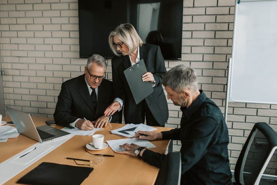 Trois professionnels quinquagénaires en réunion de travail autour de documents